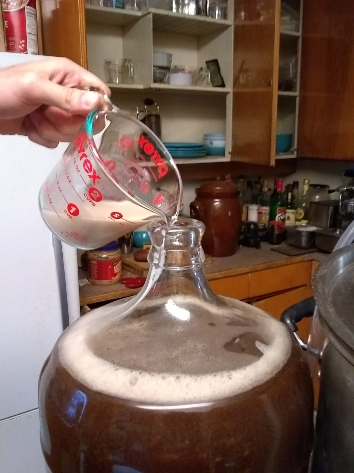 A hand pouring a measuring cup with yeast into the fermentator.