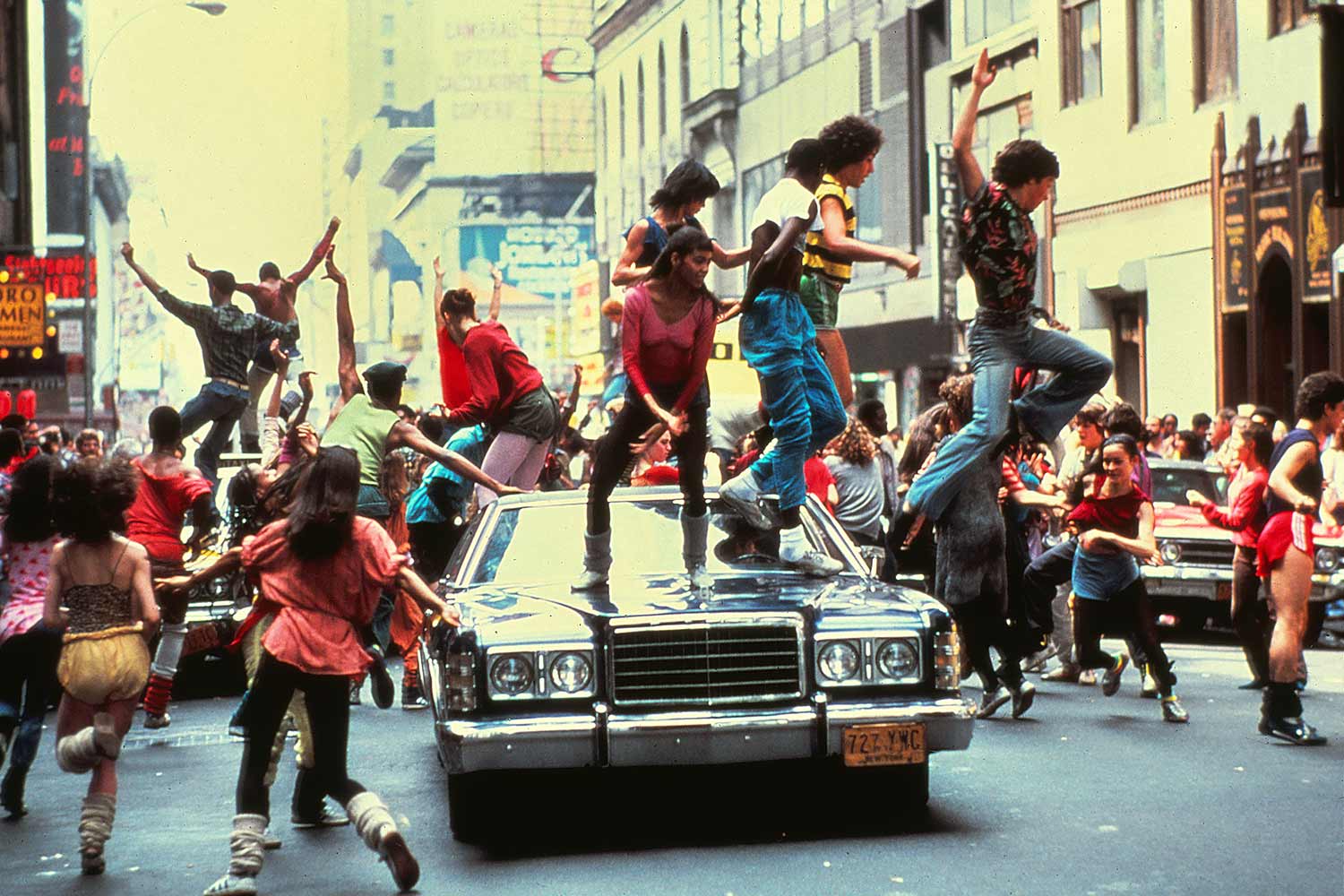 Still from the movie Fame showing people dancing on a car in New York City.