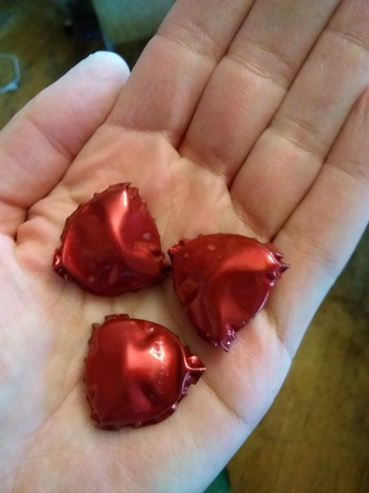 a hand showing three broken red bottle caps