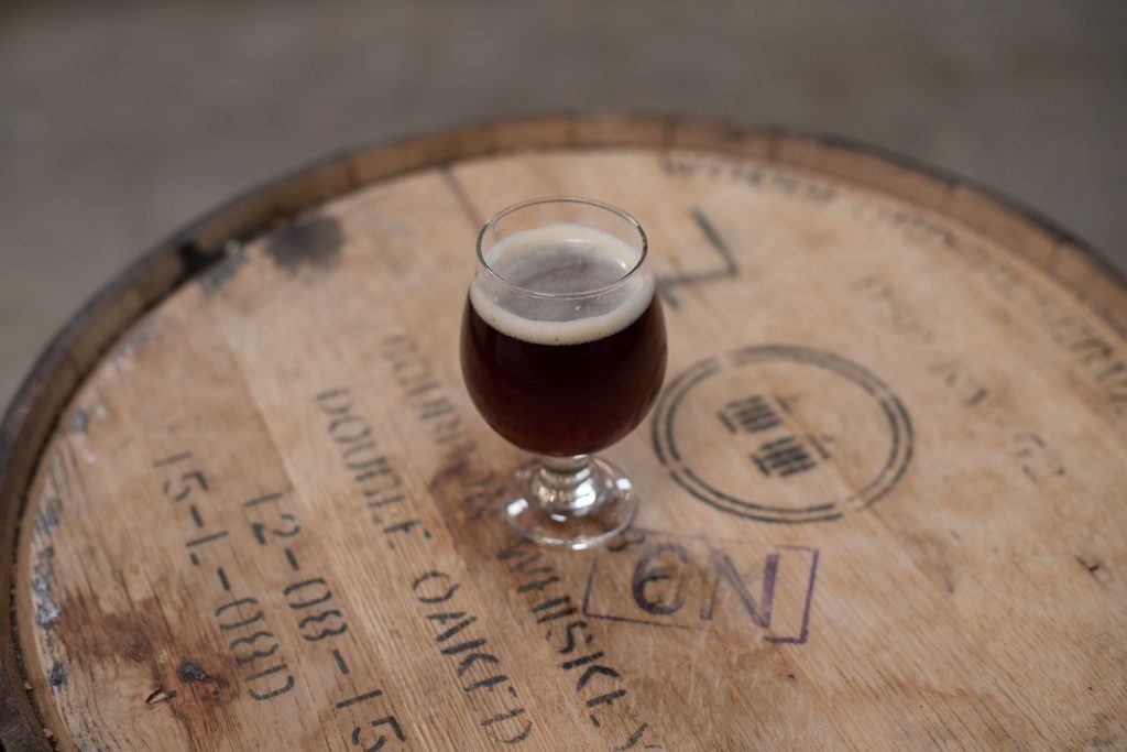 A red/brown glass of beer on a wooden barrel.