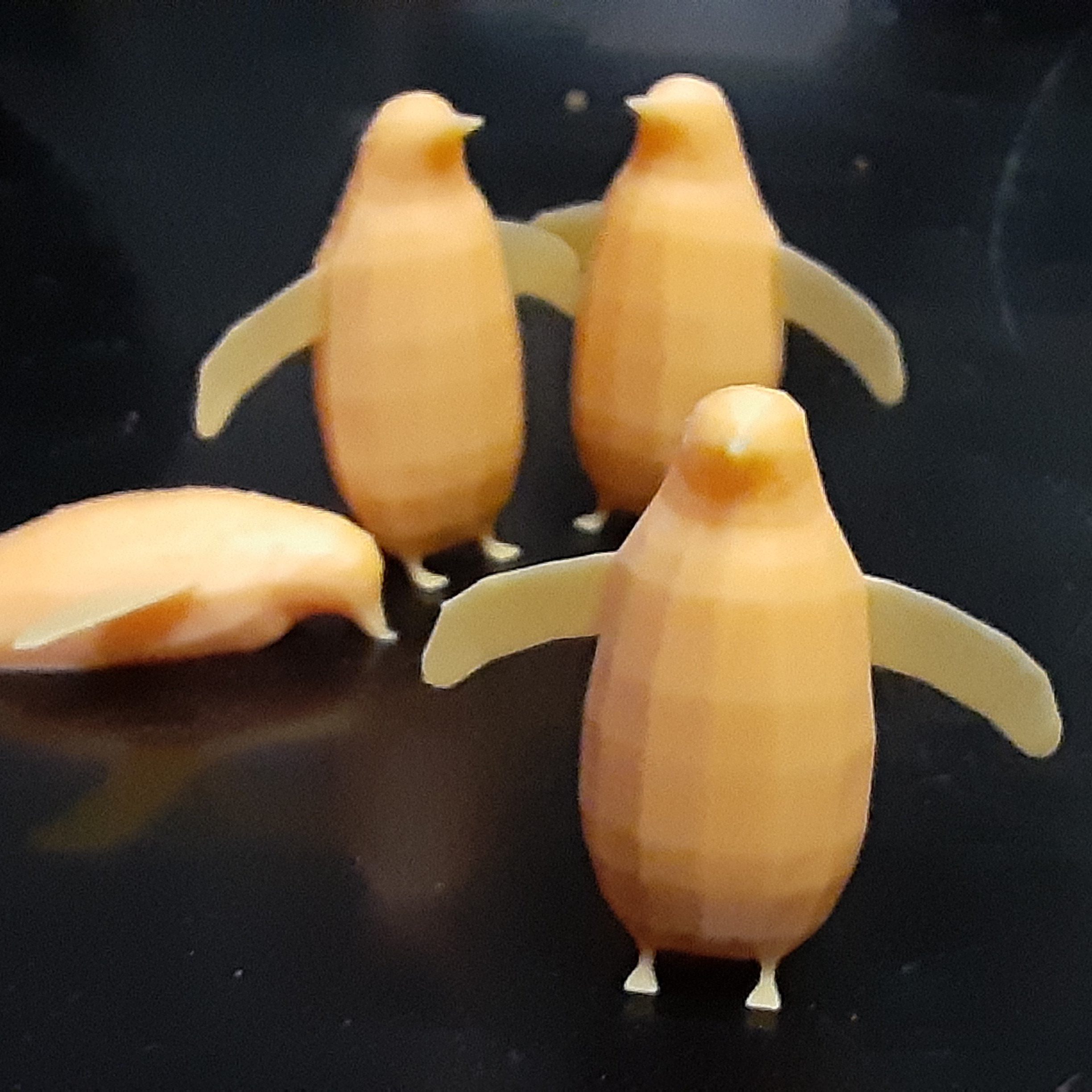 4 penguins 3D printed in orange resin. 3 are standing upright with wings spread out, one is on its belly.