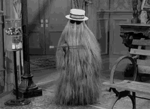 Black and White gif of Cousin Itt wearing sunglasses and a hat, twirling a stick.