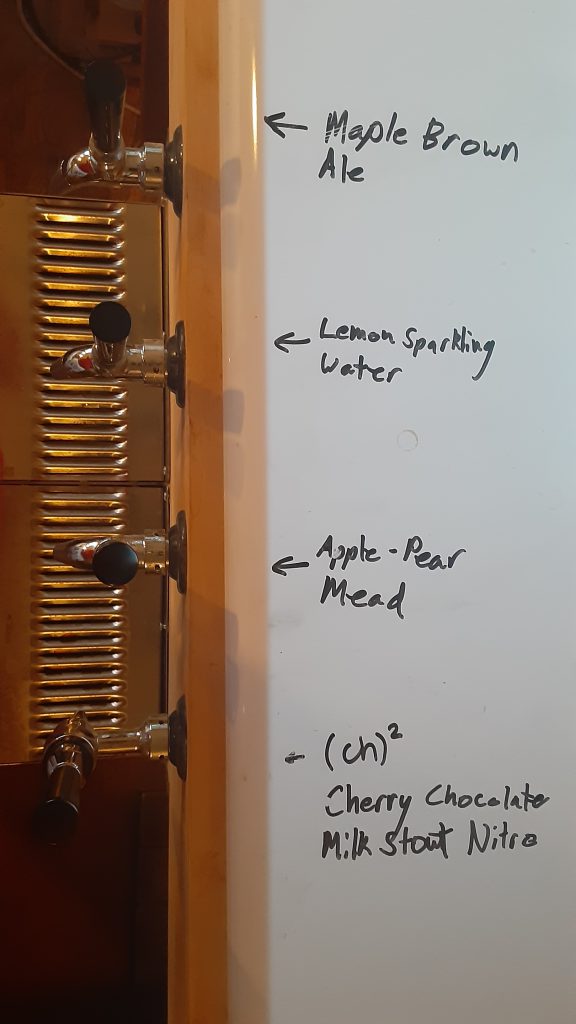 Top view of the kegerator with four taps, labels show what's on tap: Maple Brown Ale, Lemon Sparkling water, Apple-Pear Mead and (ch)^2 aka cherry chocolate milk stout nitro